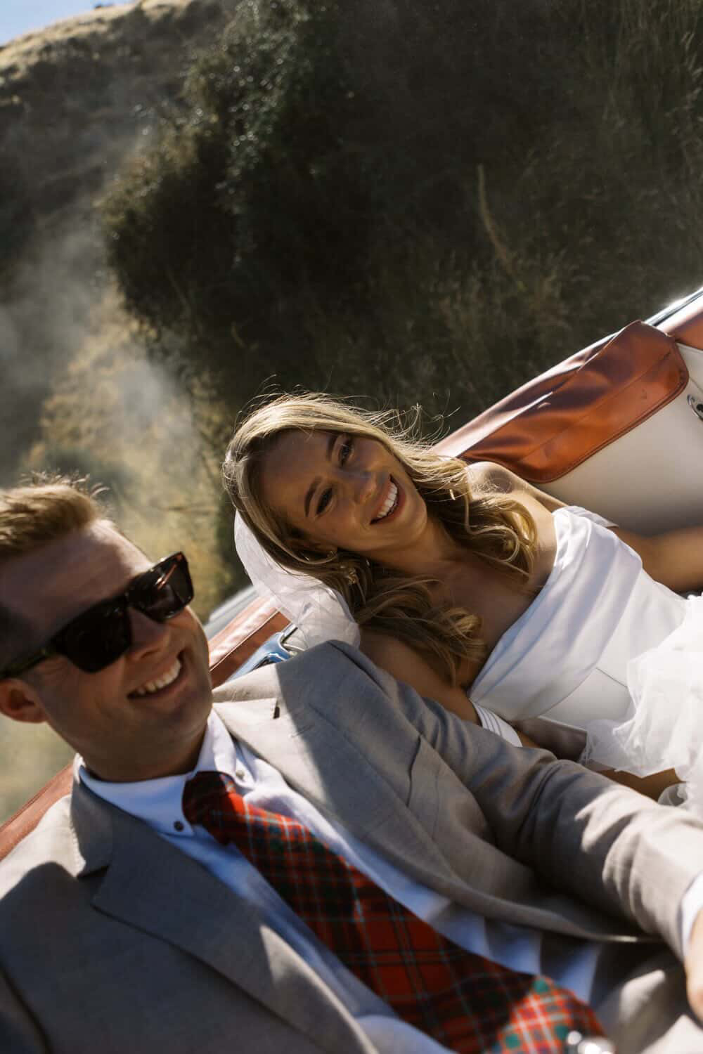 Bride and groom laughing in a vintage car