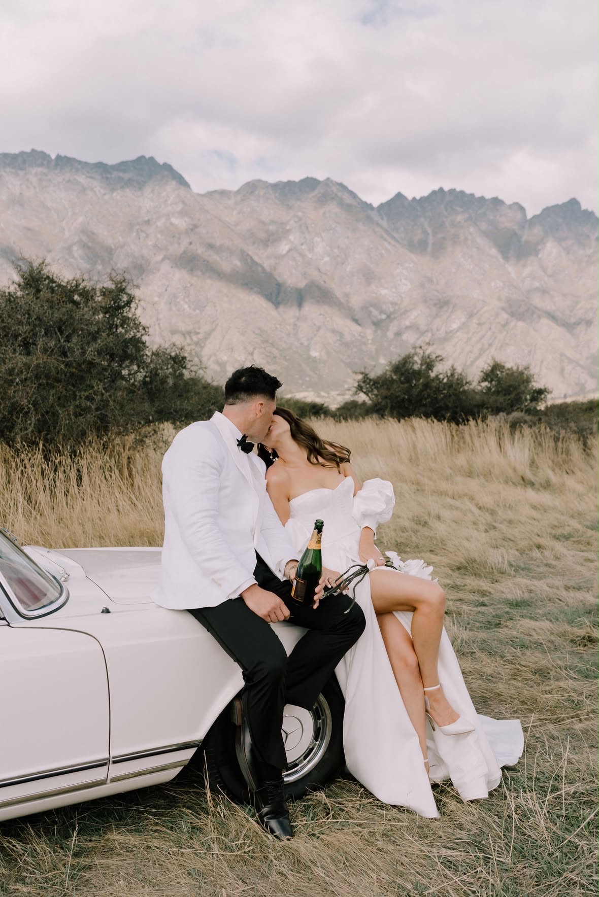 Bride and groom sharing champagne on a vintage car