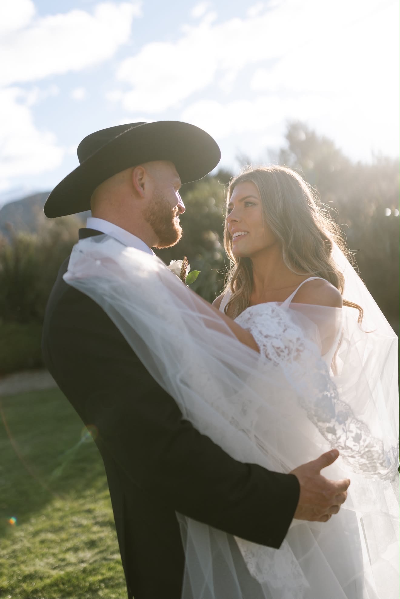 Bride and groom wrapped in her veil in the sunlight