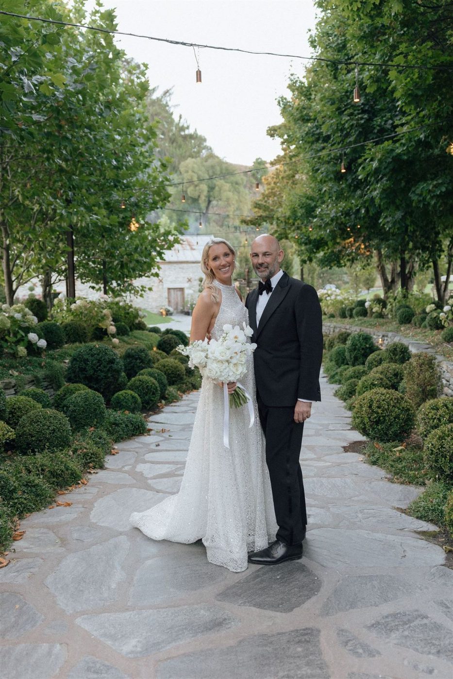Bride in a sparkling halter gown and her groom on a stone garden path