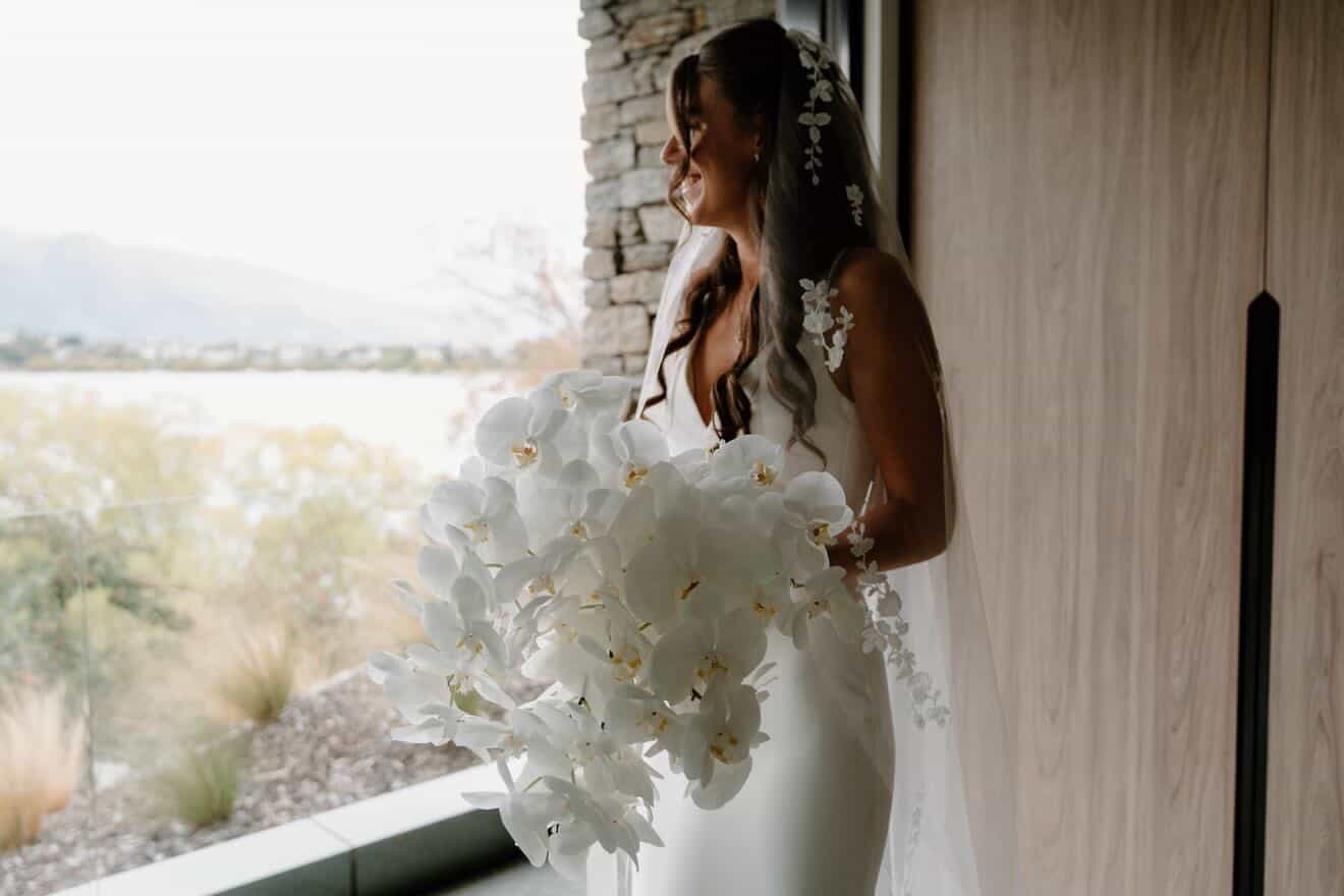 Bride with her orchid bouquet by the window