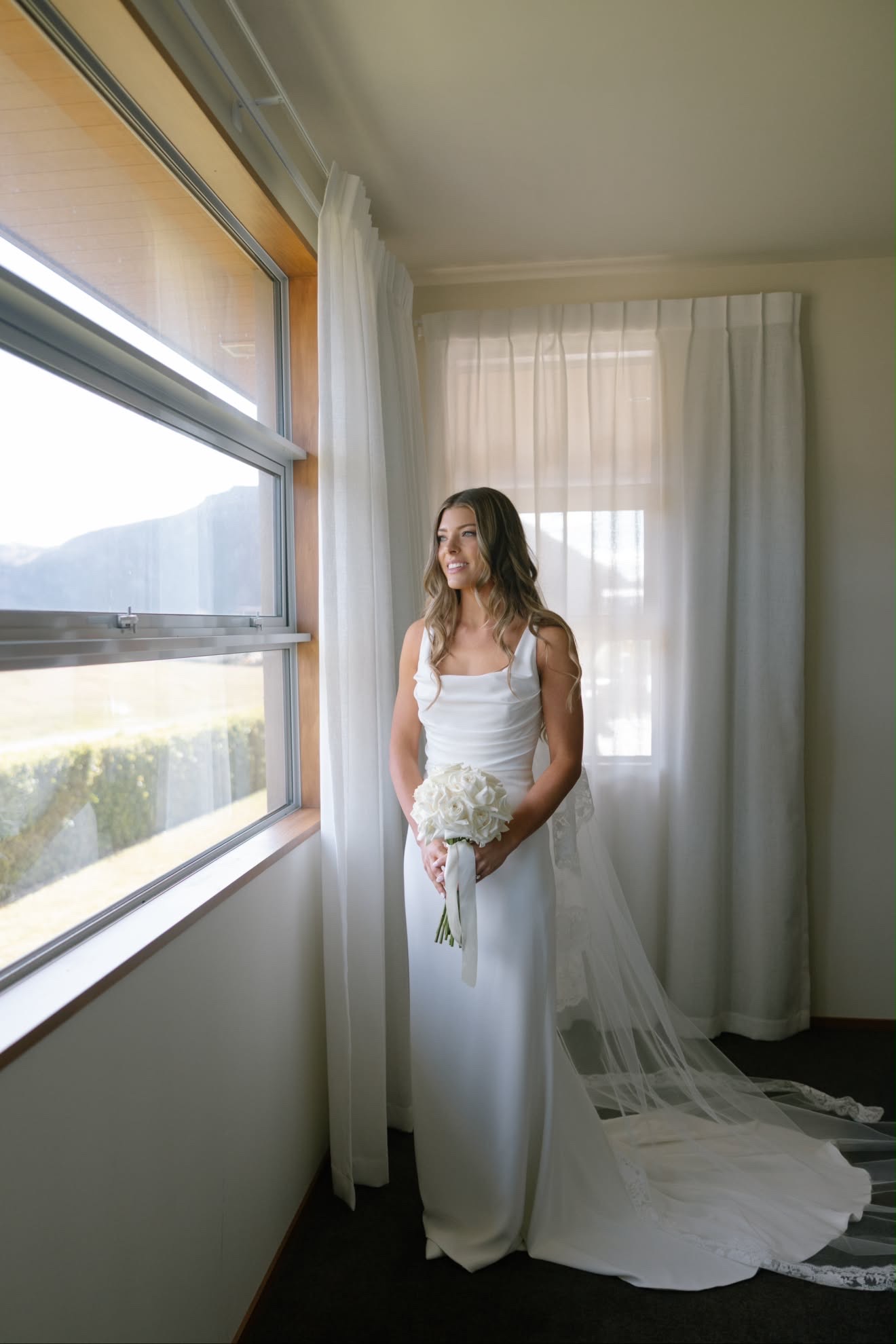 Bride standing by the window with her bouquet