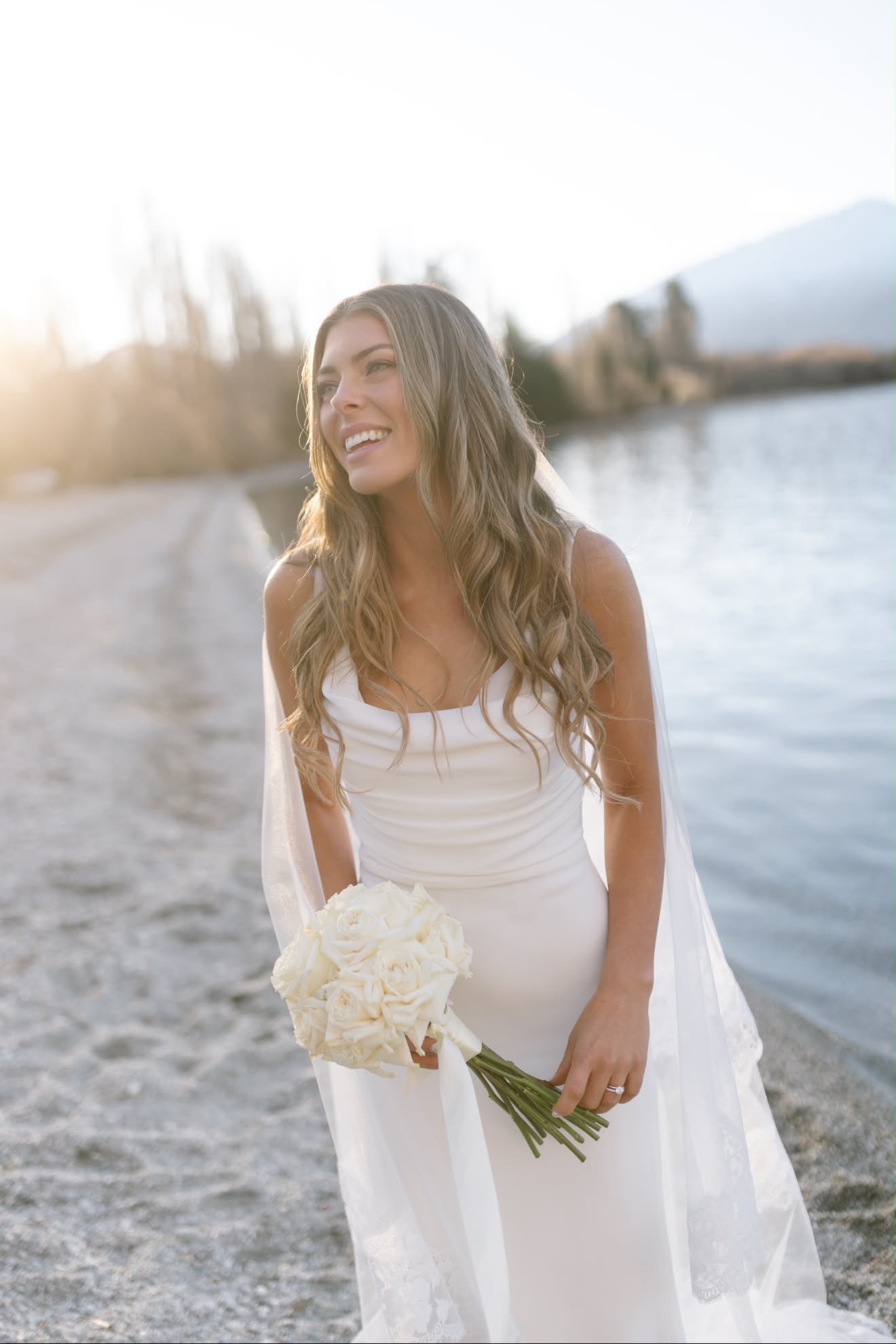 Bride smiling by the lakeshore at golden hour