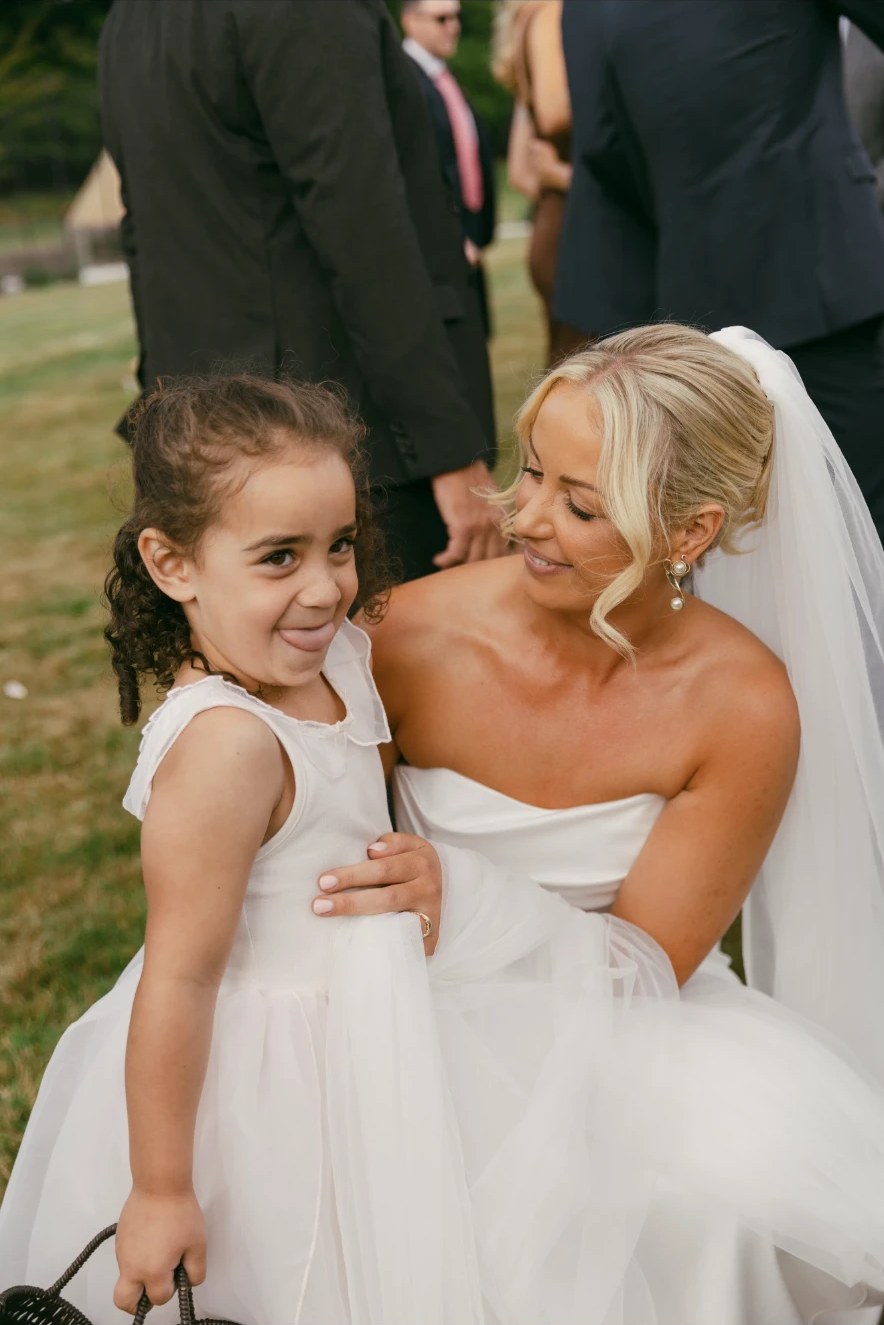 Bride crouching beside a flower girl who sticks her tongue out