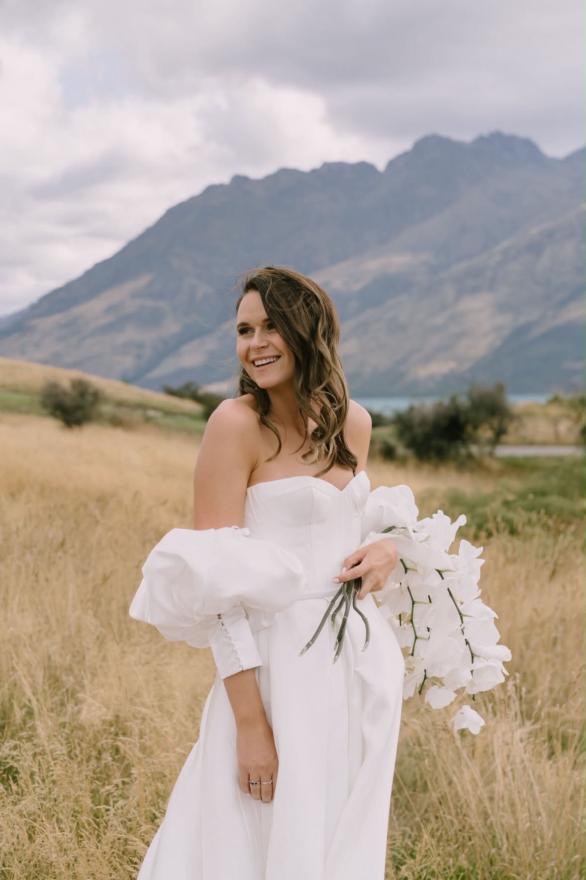 Bride laughing in the field, mountains behind