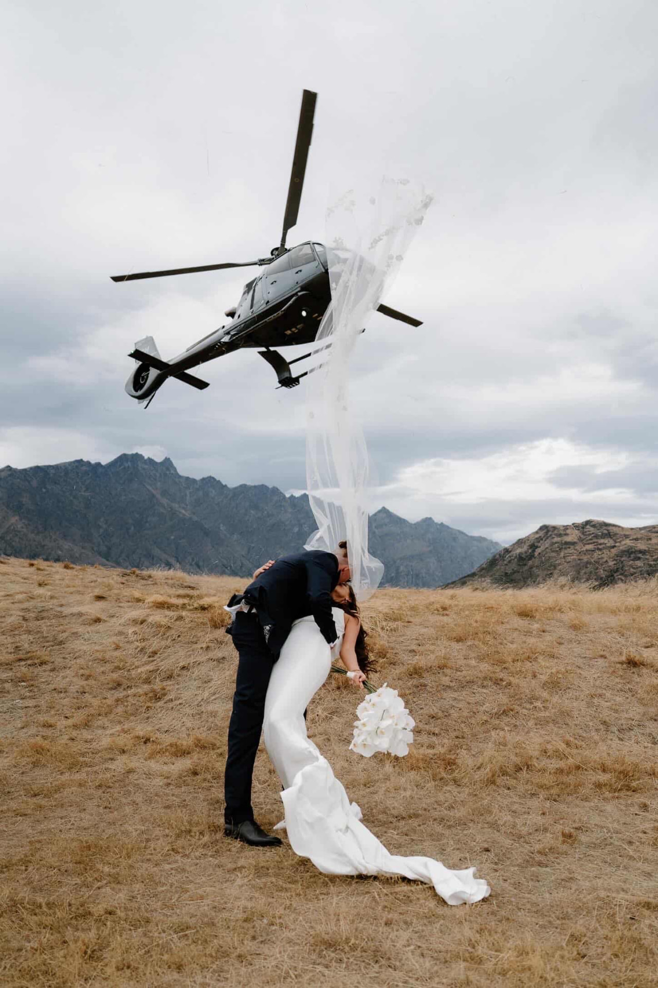 Couple kissing as a helicopter lifts off, veil flying